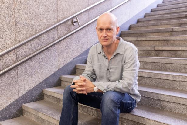 Ein Mann mit hellgrauem Hemd und Jeans sitzt auf einer Treppe.