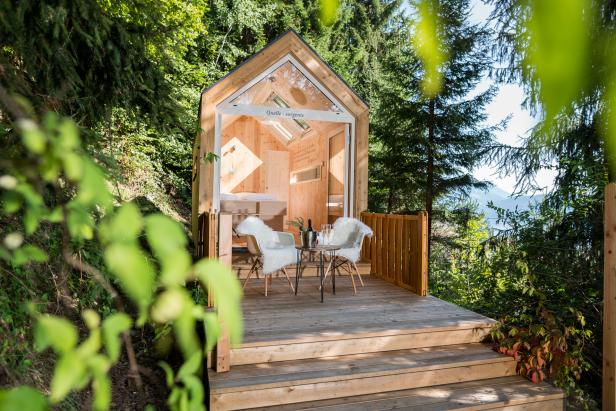 Ein kleines Holzhaus mit Terrasse, Stühlen und Blick auf die Berge.