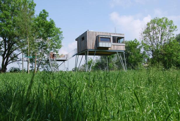 Ein hölzernes Stelzenhaus steht in einem grünen Feld.