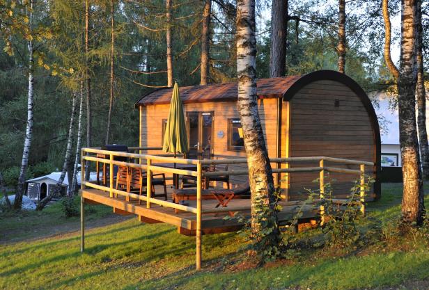 Ein hölzernes Ferienhaus mit Terrasse steht in einem Wald.