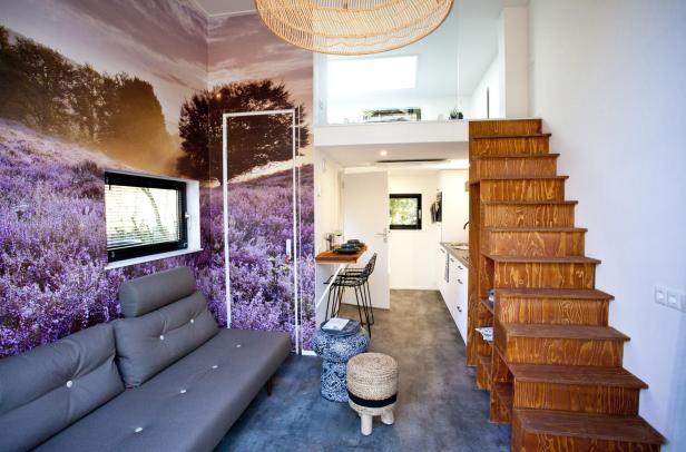 Innenansicht eines Tiny Houses mit Sofa, Treppe zum Schlafbereich und einer Fototapete mit Lavendelmotiv.