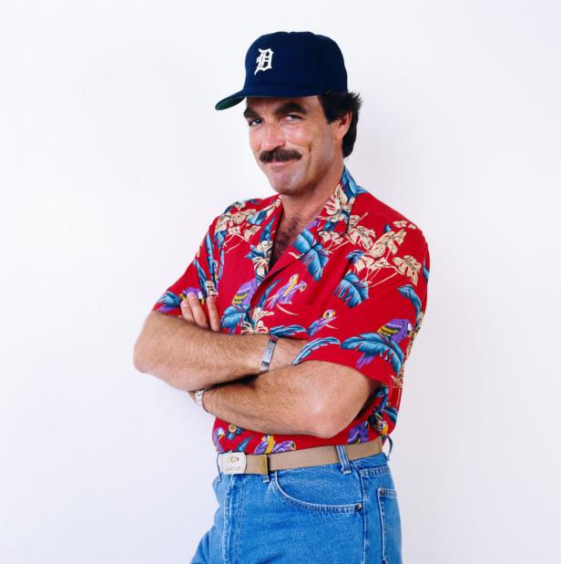 Tom Selleck mit Schnurrbart, Baseballkappe und Hawaiihemd vor einer weißen Wand.