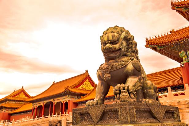 Eine bronzene Löwenstatue vor traditionellen chinesischen Gebäuden.