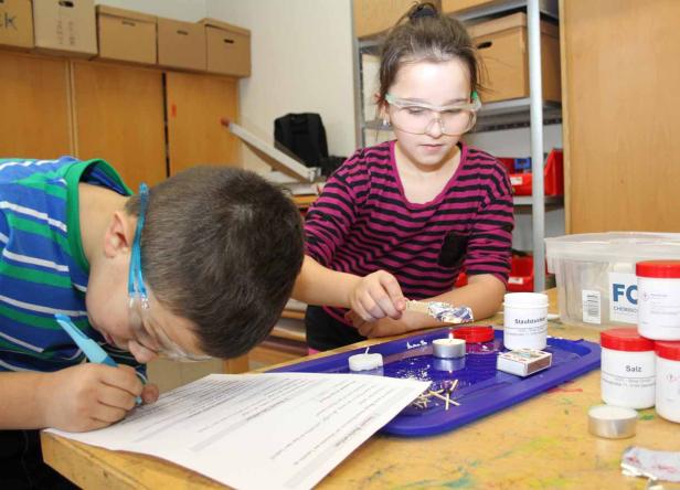 Zwei Kinder mit Schutzbrillen experimentieren mit Kerzen und Chemikalien im Unterricht.