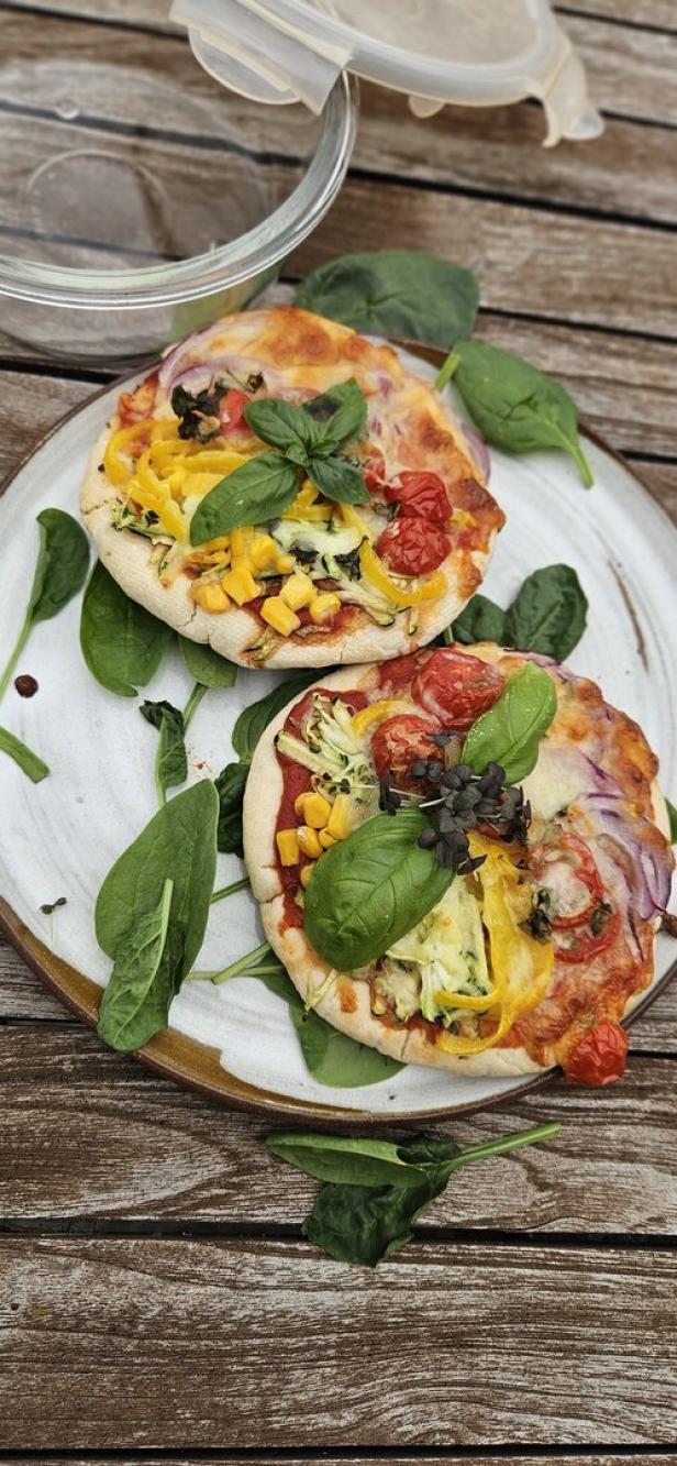 Zwei Mini-Pizzen mit Gemüse und Basilikum auf einem Teller.