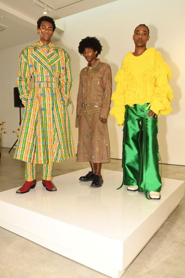 Drei Models präsentieren farbenfrohe und extravagante Mode auf einem weißen Podest.