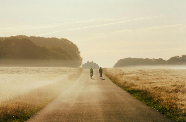 Zwei Radfahrer fahren auf einer Straße durch eine neblige Landschaft.