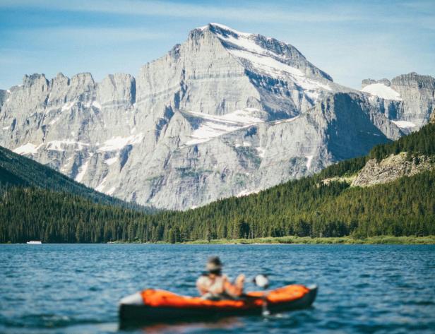 Eine Person paddelt in einem Kanu auf einem See vor einer Bergkulisse.
