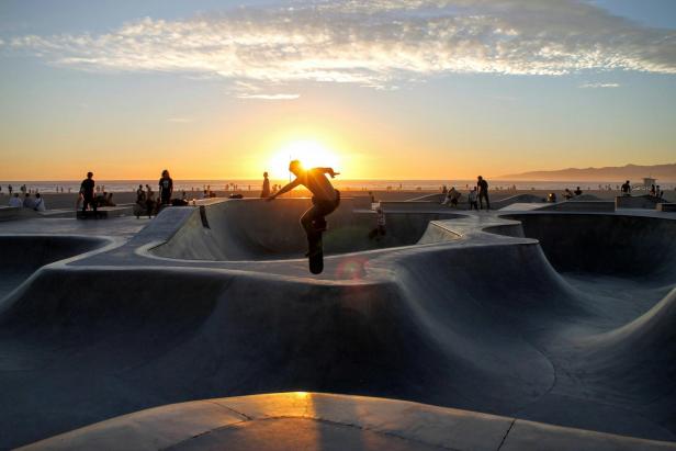 Ein Skateboarder springt in einem Skatepark vor einem Sonnenuntergang.