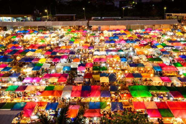 Luftaufnahme des Ratchada Rot Fai Nachtmarkts in Bangkok, beleuchtet und lebhaft, mit zahlreichen Ständen und Besuchern