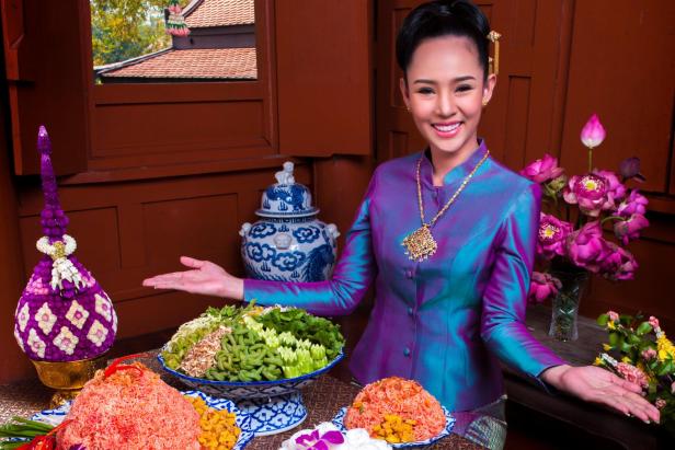 Eine Frau in lila Kleid zeigt traditionelle thailändische Speisen