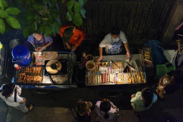 Eine Ansammlung von Personen um einen Essensstand in Bangkok, der beliebte Streetfood-Gerichte serviert