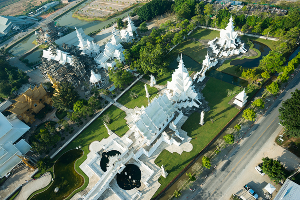 Blick von oben auf den weißen Tempel Wat Rong Khun, der in einem Park steht und traditionelle sowie moderne buddhistische Stile kombiniert