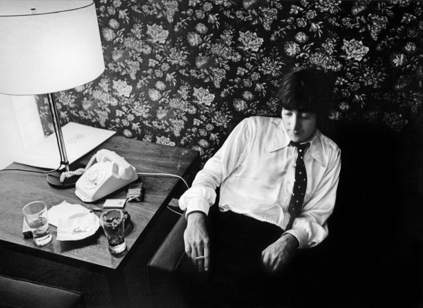 John Lennon sitzt mit einer Zigarette in einem Sessel.