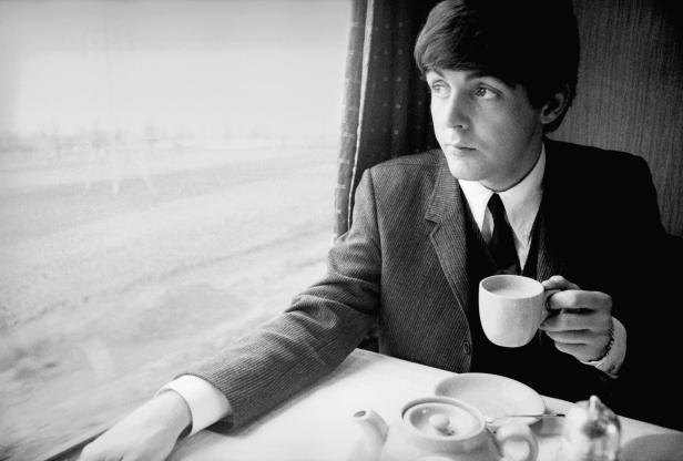 Paul McCartney sitzt in einem Zug und hält eine Tasse in der Hand.