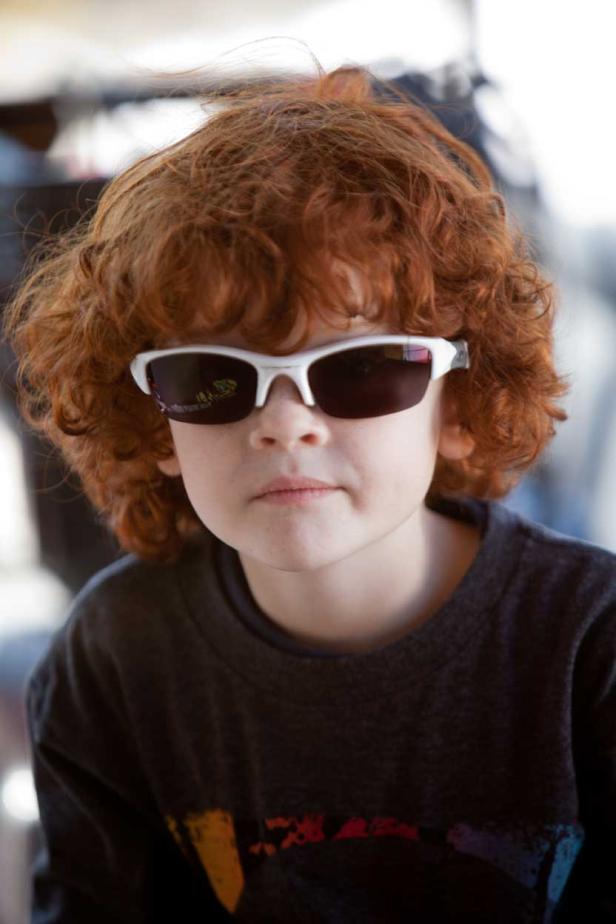 Ein Junge mit roten Locken und Sonnenbrille blickt in die Kamera.