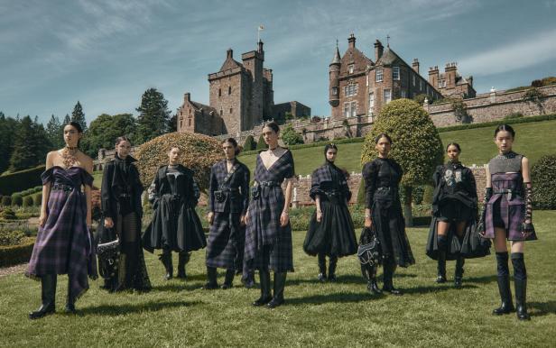 Eine Gruppe von Models präsentiert Mode vor einem Schloss auf einer grünen Wiese.