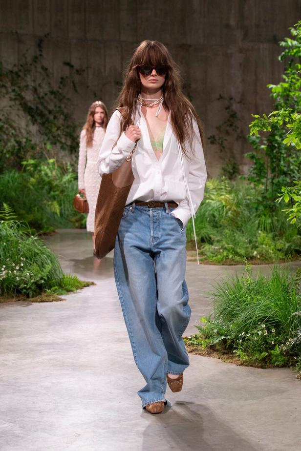 Eine Frau mit Sonnenbrille und übergroßen Jeans läuft auf einem Laufsteg.