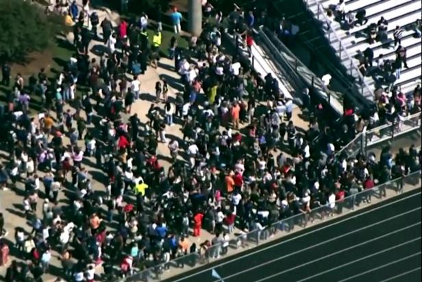 Students and staff gather next to the football field after law enforcement officers responded to a fatal shooting at Apalachee High School