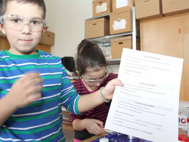 Zwei Kinder mit Schutzbrillen führen Experimente mit Wachs, Salz und Zucker durch.