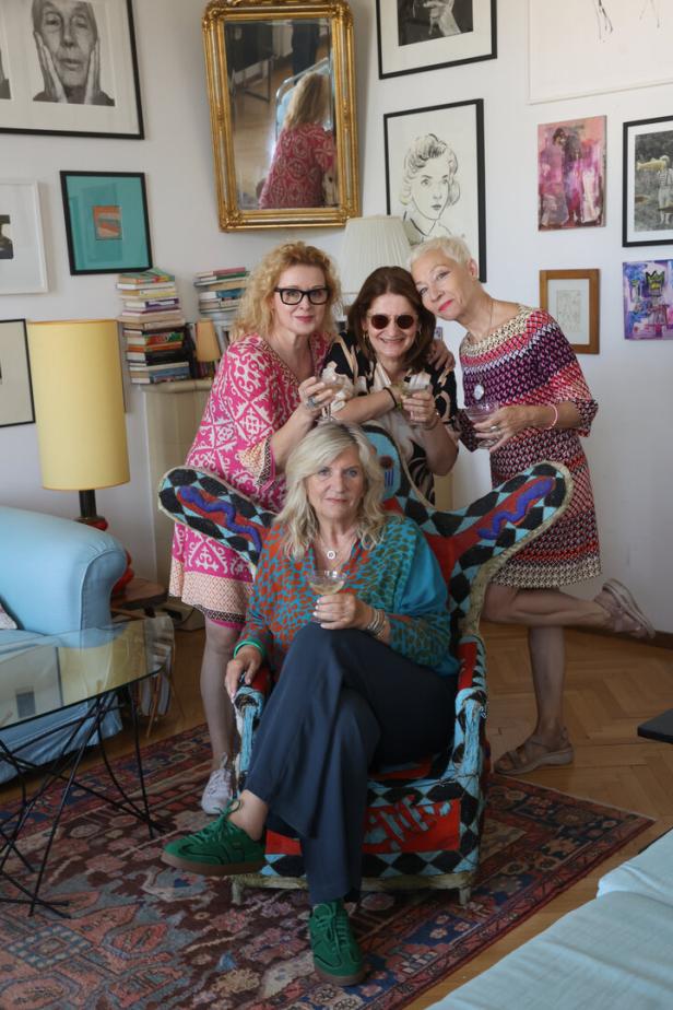 Vier Frauen posieren mit Weingläsern in einem Wohnzimmer mit Kunst an den Wänden.