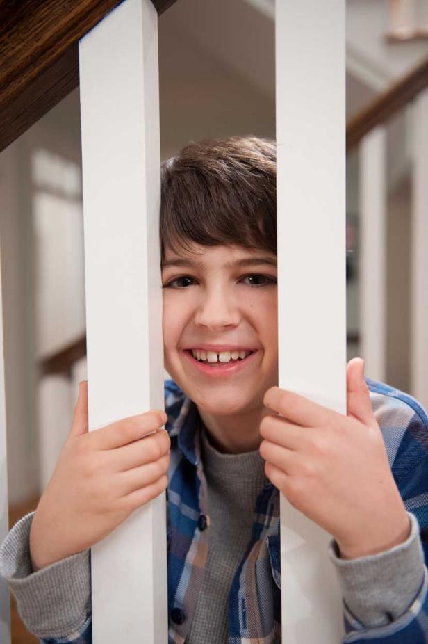 Ein lächelnder Junge schaut durch die Sprossen eines Treppengeländers.