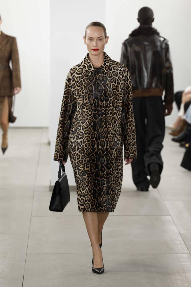 Eine Frau in einem Leopardenmantel und schwarzen Schuhen läuft auf einem Laufsteg.