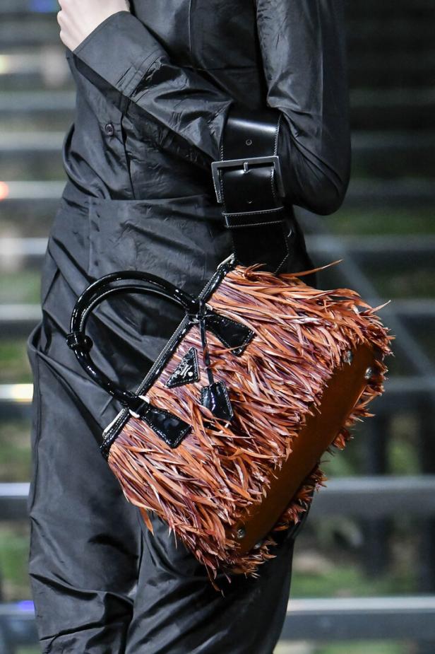 Eine Person mit einer Prada-Handtasche mit Fransen über der Schulter.