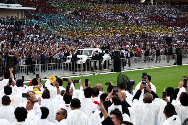 Eine Menschenmenge jubelt einem Papamobil in einem Stadion zu.