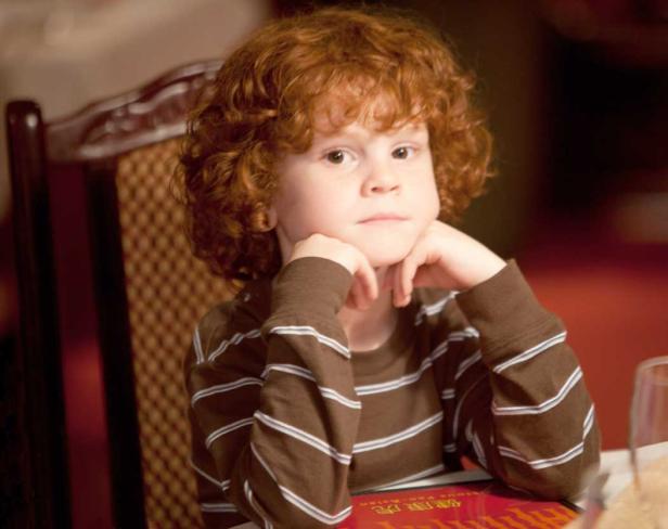 Ein nachdenklicher Junge mit roten Locken sitzt an einem Tisch.