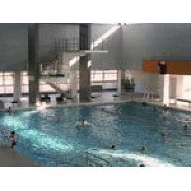 Innenansicht eines Schwimmbads mit mehreren Schwimmern und einem Sprungturm.
