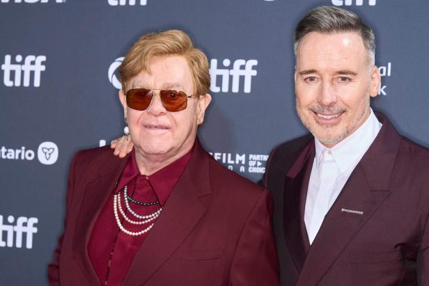 Elton John und David Furnish posieren gemeinsam vor einer Wand mit dem Logo des Toronto International Film Festival.
