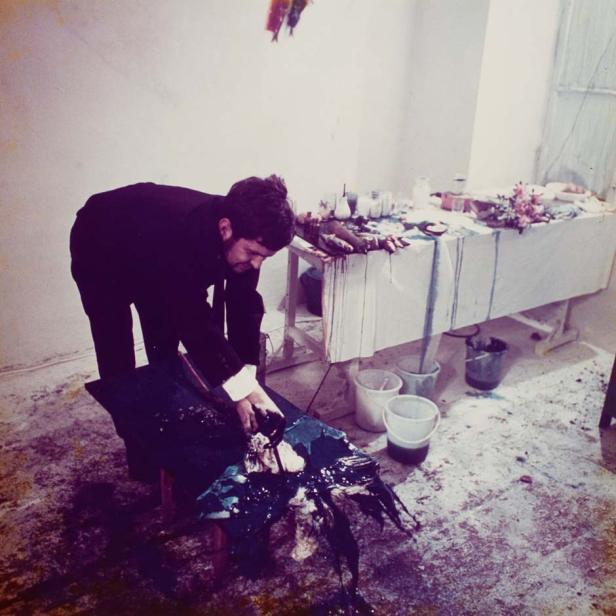 Ein Mann im Anzug arbeitet an einem mit Farbe bedeckten Kunstwerk in einem Atelier.