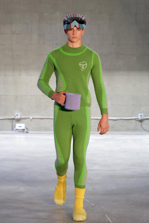 Ein Mann in grüner Sportbekleidung und Skibrille hält eine Tasse.
