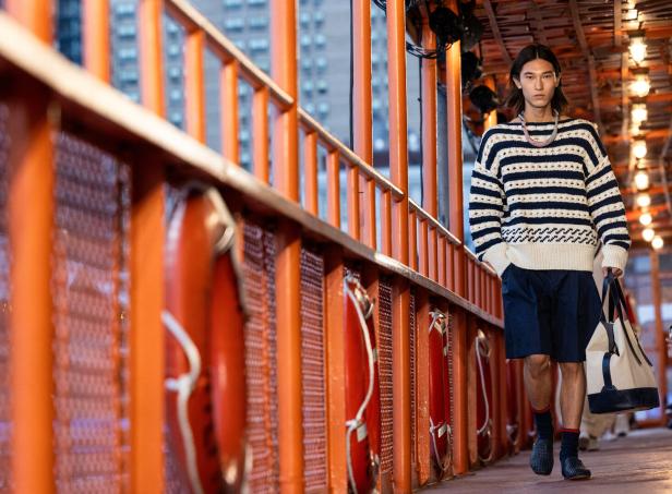 Ein Mann mit einem gestreiften Pullover und Shorts geht an einer orangefarbenen Reling entlang.