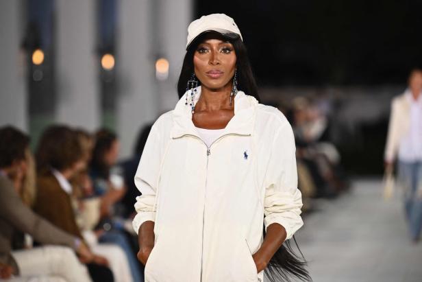 Naomi Campbell auf dem Laufsteg in einer weißen Jacke und passender Kappe.