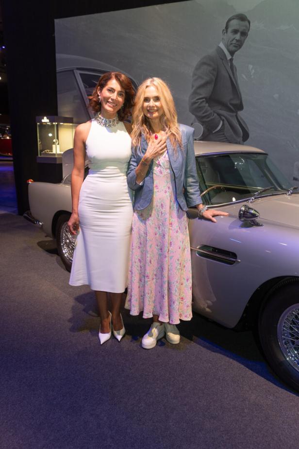 Zwei Frauen posieren vor einem Aston Martin und einem Porträt von Sean Connery als James Bond.
