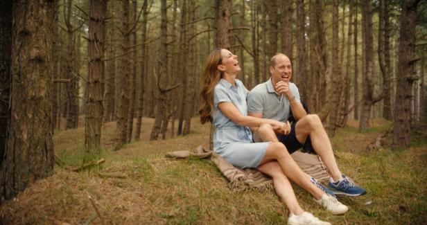 Prinz William und Prinzessin Kate sitzen lachend auf einer Decke im Wald.