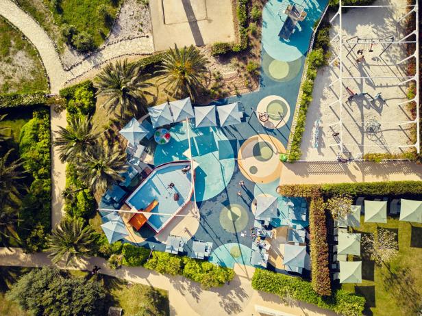 Ein Spielplatz mit Pool, Sonnenschirmen und verschiedenen Spielgeräten von oben.