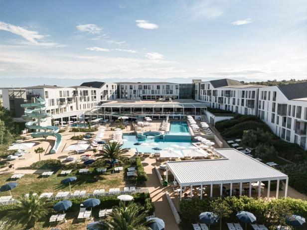 Luftaufnahme eines Resorts mit Pools, Wasserrutsche und Liegestühlen.