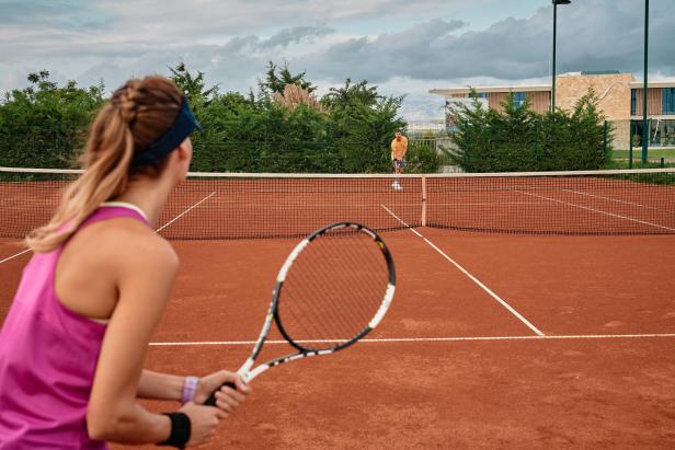 Eine Frau mit Tennisschläger beim Tennisspiel auf einem Sandplatz.