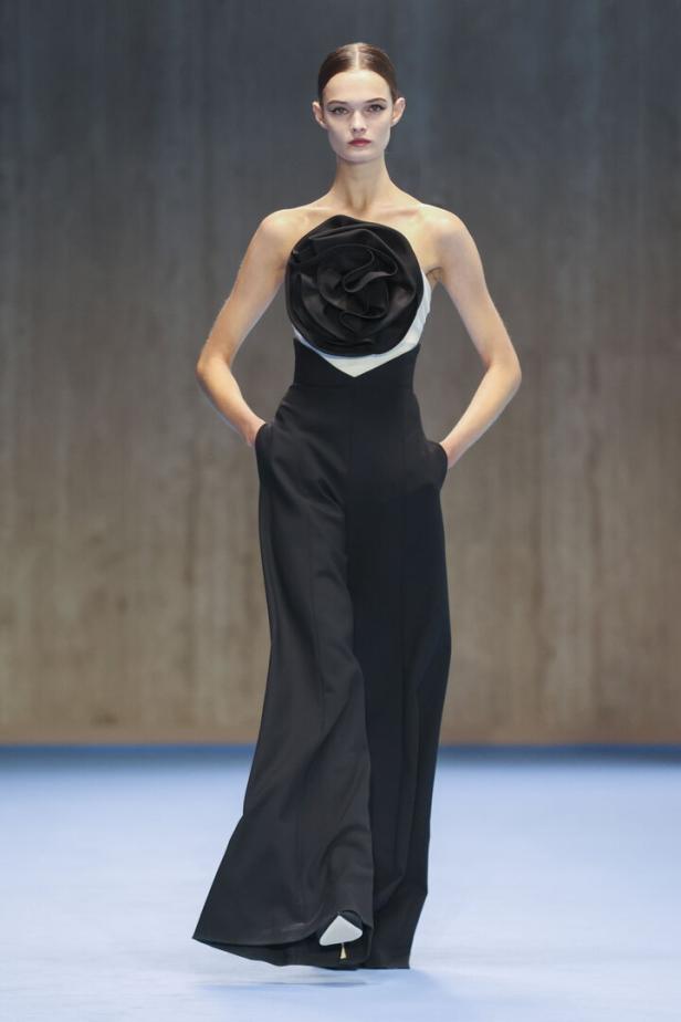 Ein Model präsentiert ein schwarzes, ärmelloses Hosenkleid mit einer großen Stoffrose von Carolina Herrera.