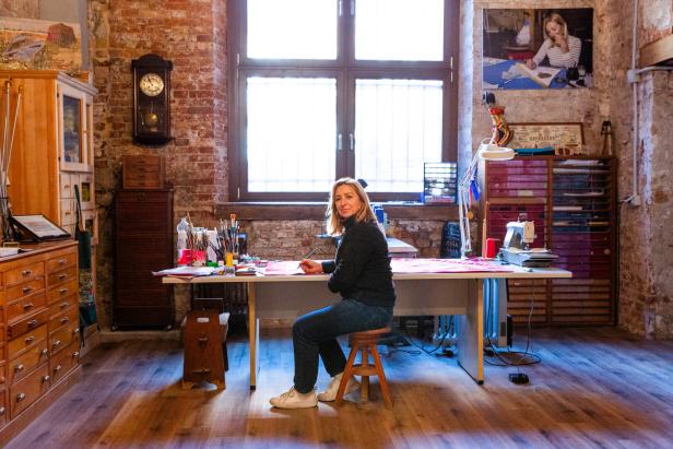 Eine Frau sitzt an einem Tisch in einem Atelier und malt.