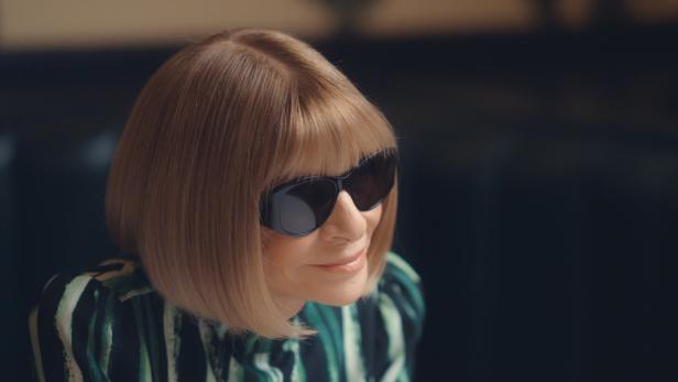 Anna Wintour mit Sonnenbrille und blondem Bob, lächelnd.