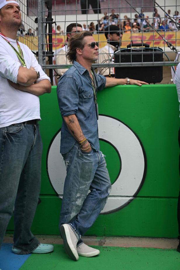 Brad Pitt lehnt an einer grünen Mauer und schaut in die Ferne.