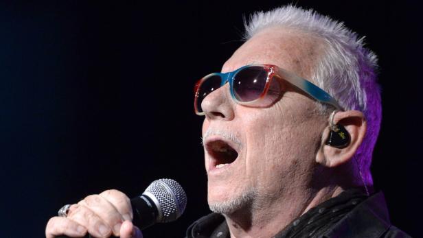 Ein älterer Mann mit Sonnenbrille singt in ein Mikrofon.