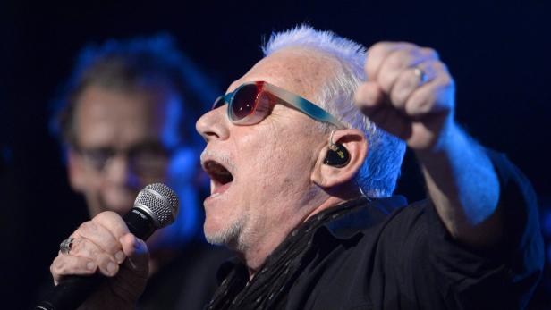 Ein älterer Mann mit Sonnenbrille singt mit erhobener Faust in ein Mikrofon.