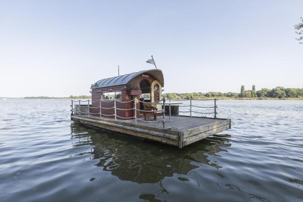 Ein kleines Hausboot mit dem Namen „Hermann“ auf einem See.