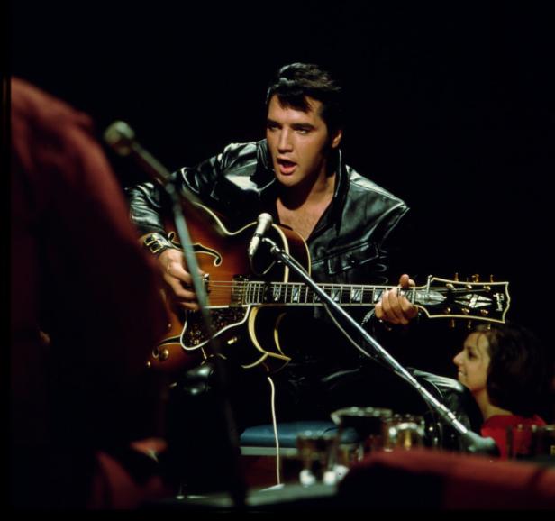 Elvis Presley spielt Gitarre in einem schwarzen Lederanzug.