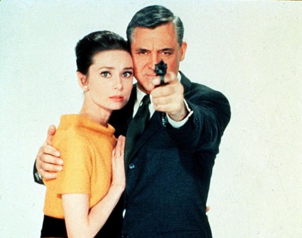 Cary Grant zielt mit einer Pistole, während Audrey Hepburn daneben steht.
